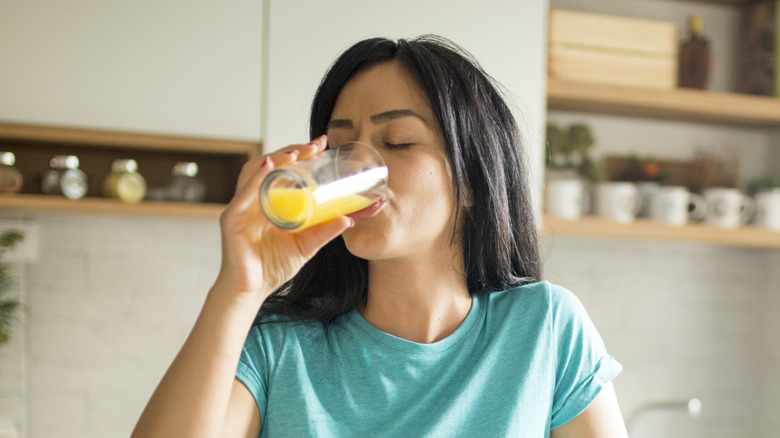 A young woman drinking a glass of yellow liquid