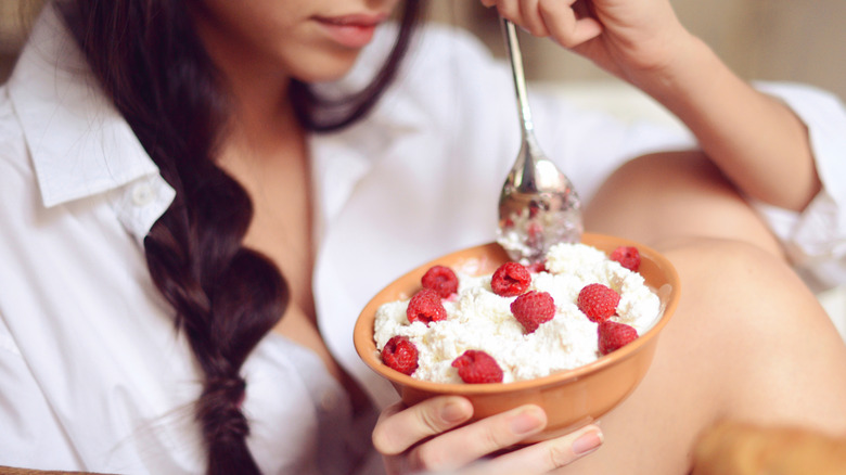 woman's hands holding a bowl of cottage cheese with strawberries