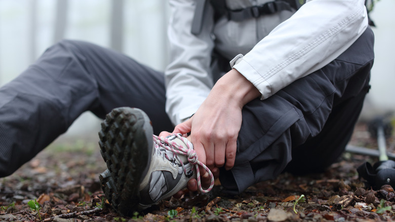 A hiker out in nature grabbing their injured ankle