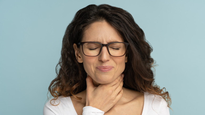 Young woman with glasses holding her throat in pain 