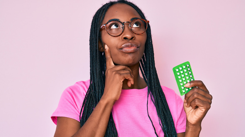 Perplexed woman holding birth control pills