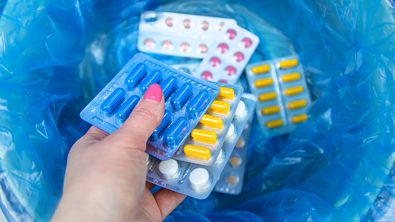 Hand dropping a pack of medication into a trash bin