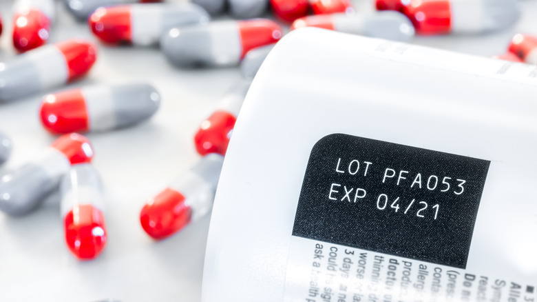 Close up on a bottle of medication's expiration date surrounded by pill capsules