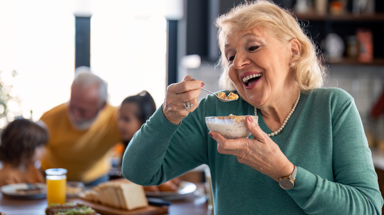 older woman eating oatmeal with family behind her