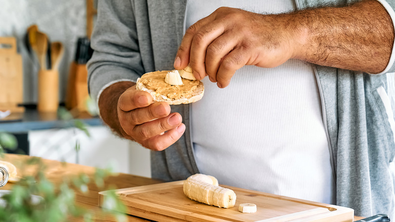 man's hand adding banana slices to peanut butter rice cake