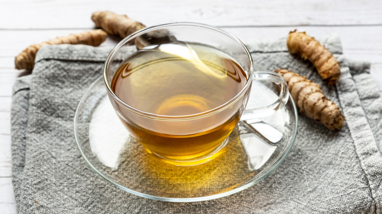 A glass cup of turmeric tea with turmeric root