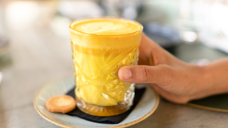 A woman's hand holding a glass of golden milk with turmeric