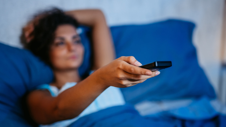 A woman lying in bed watching TV with a remote control in her hand