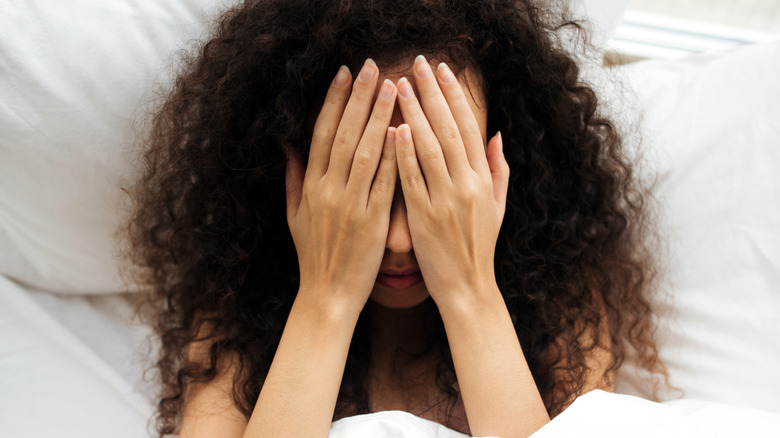 A woman lying in bed covering her face