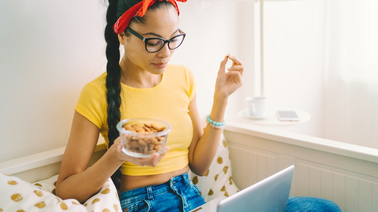 woman eating a bowl of almonds while working on her laptop