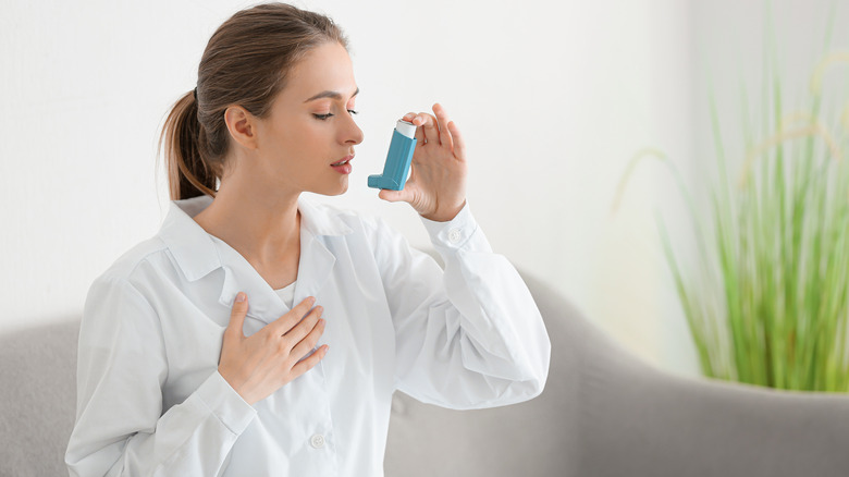 Woman sitting on white couch about to use an inhaler