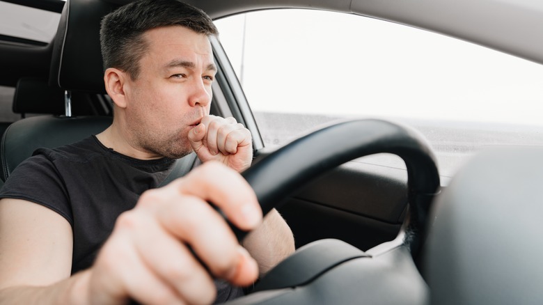 man coughing inside his car