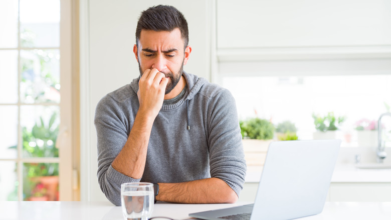 A stressed man bites her nails by a computer