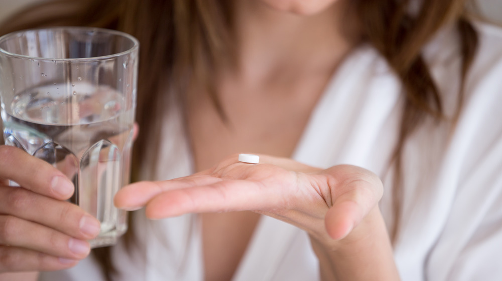 Person holding pill in one hand and glass of water in the other