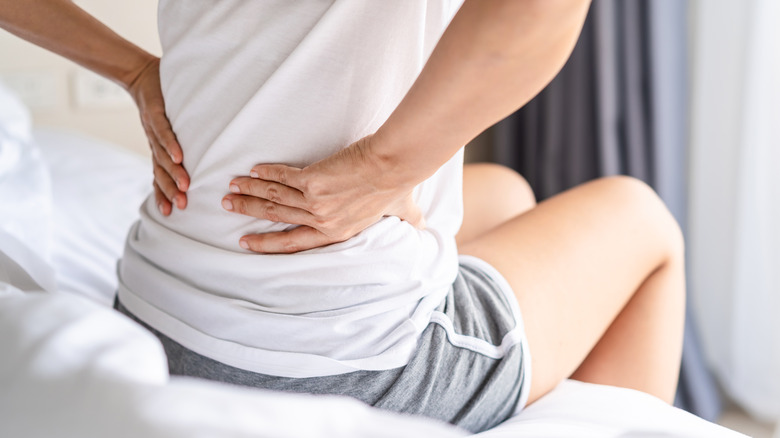 Woman sitting at edge of bed holding lower back in pain