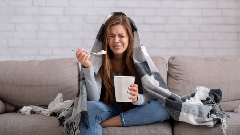 heartbroken young woman eating ice cream on the couch while crying 