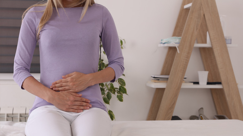 Woman patient waiting on exam table at doctor's office holding her abdomen 