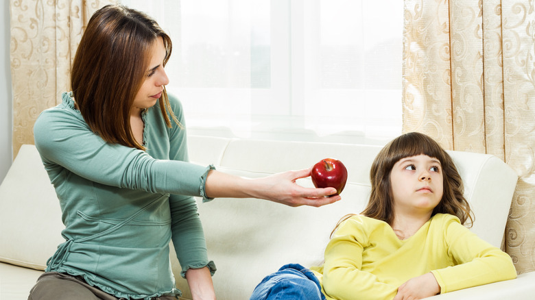A mom tries to get her daughter to eat an apple