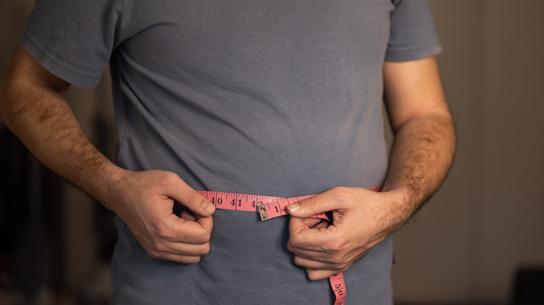 man measuring waist to see if he has lost weight