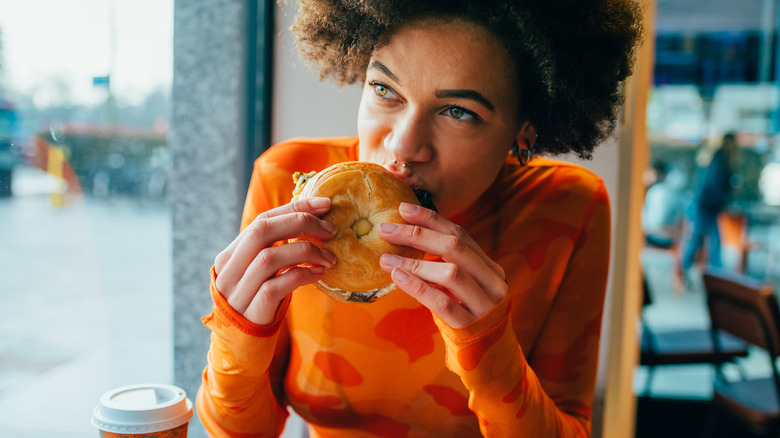 A woman eats a bagel in a coffee shop