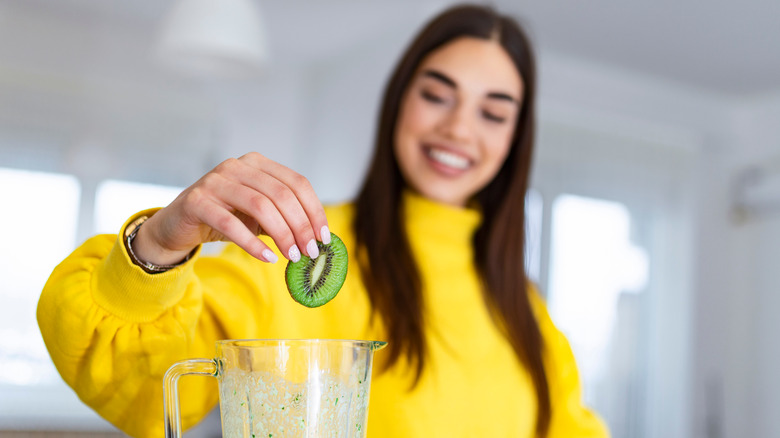 Woman dropping kiwi into blender