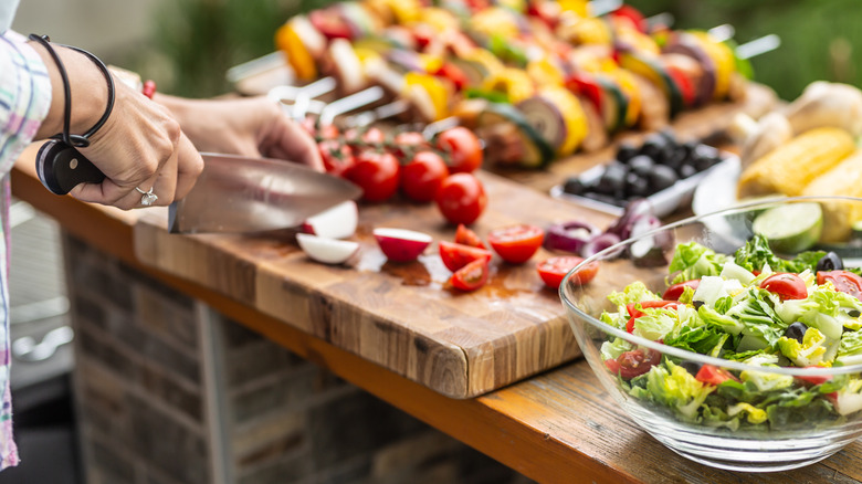 A table of salad, kabobs, corn, olives for a cookout