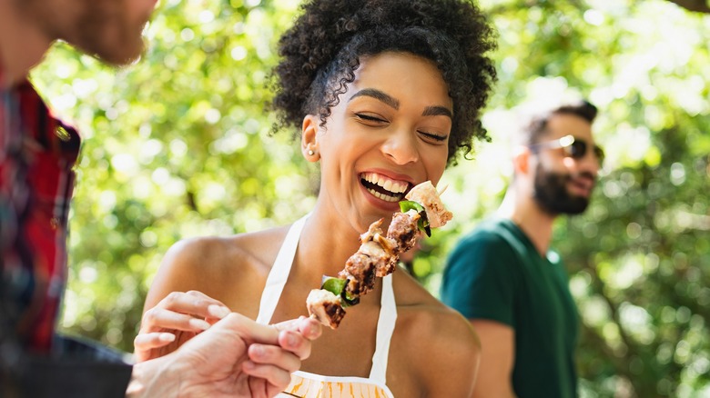 Young woman being fed meat skewer