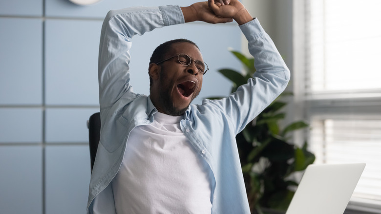 Man in glasses yawning while working at a computer