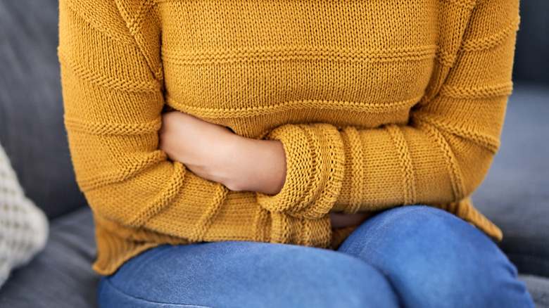 Woman sitting on couch holding stomach