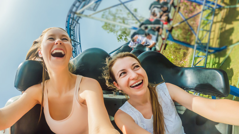 two young women smiling and laughing on a roller coaster 