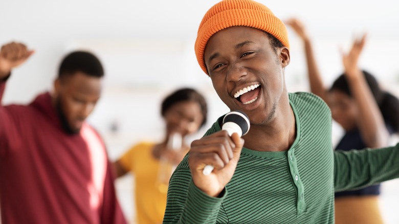 Young man singing into a microphone and dancing with friends