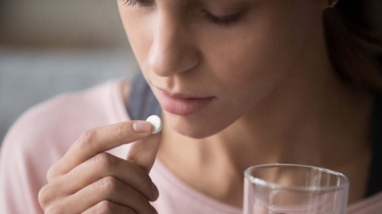 girl taking white tablet with water