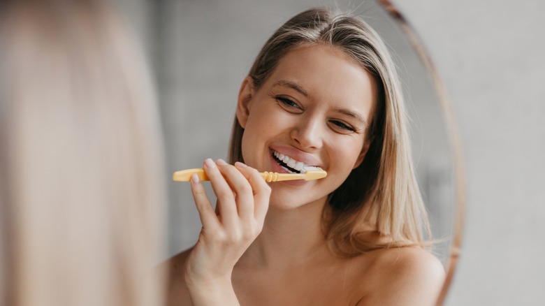 woman brushing teeth in mirror