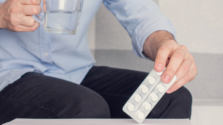 Man holding white pills and glass