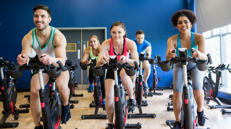 Five people taking a spin class in a room with a blue wall and windows