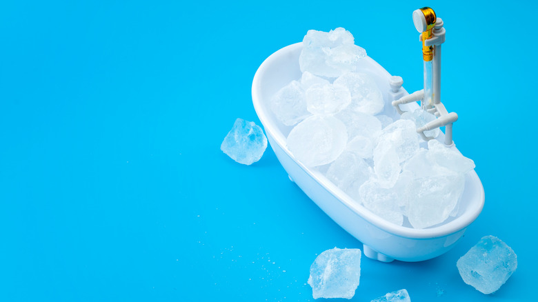 Bathtub full of ice cubes on blue background 