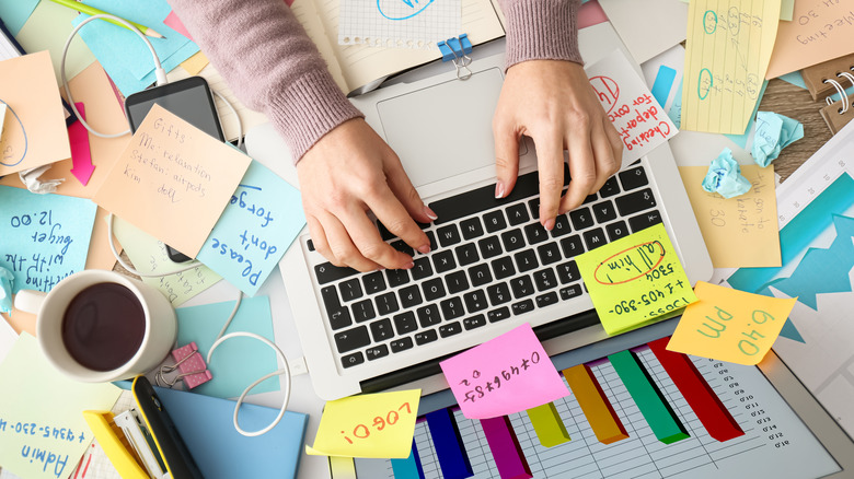 Fingers on keyboard atop cluttered desk