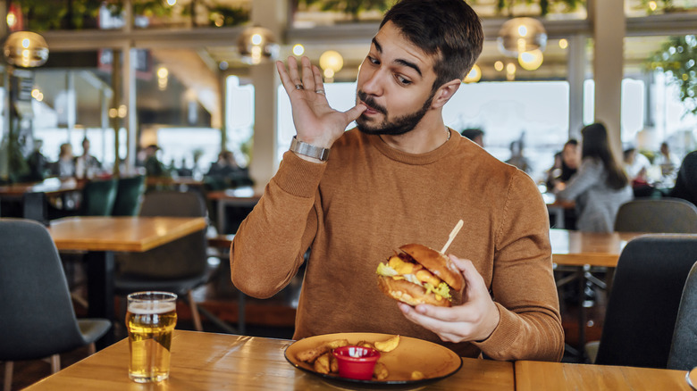 man eating a cheeseburger and drinking a beer