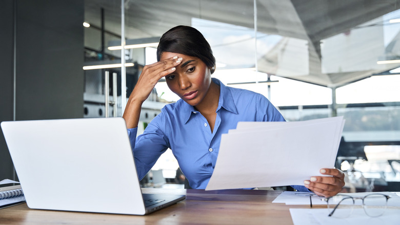 A stressed woman at work holding her temple as she looks over papers