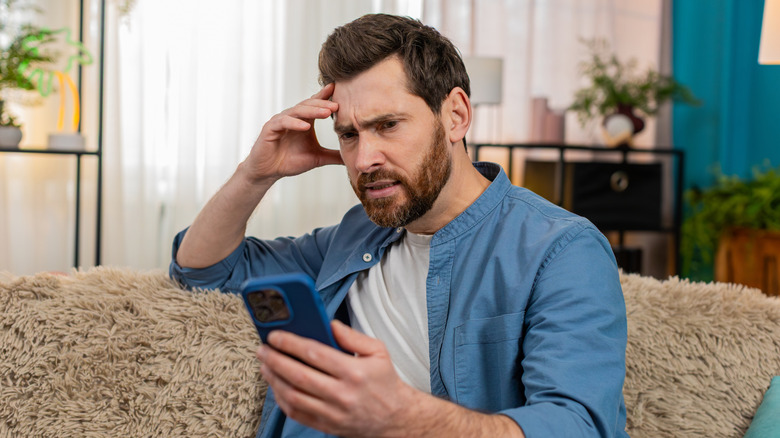 A man with an anxious look while reading on his phone