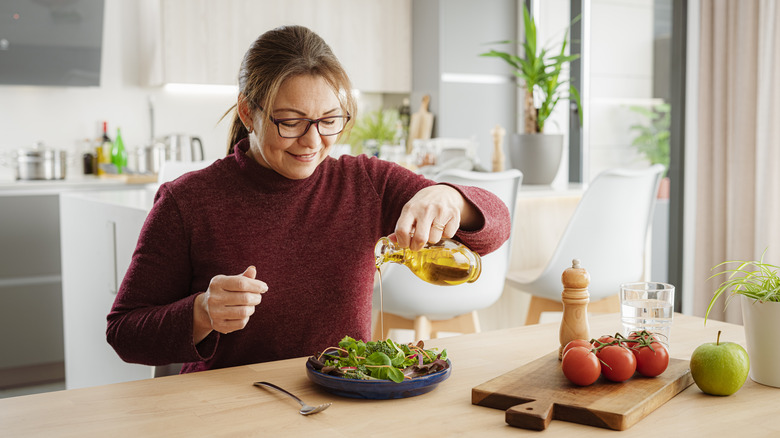 Woman pouring olive oil over salad