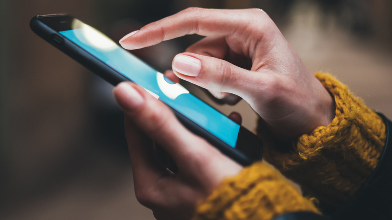Pair of hands holding smart phone and tapping screen