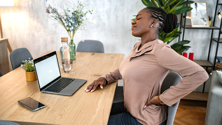 A woman experiencing lower back pain while working from a home desk
