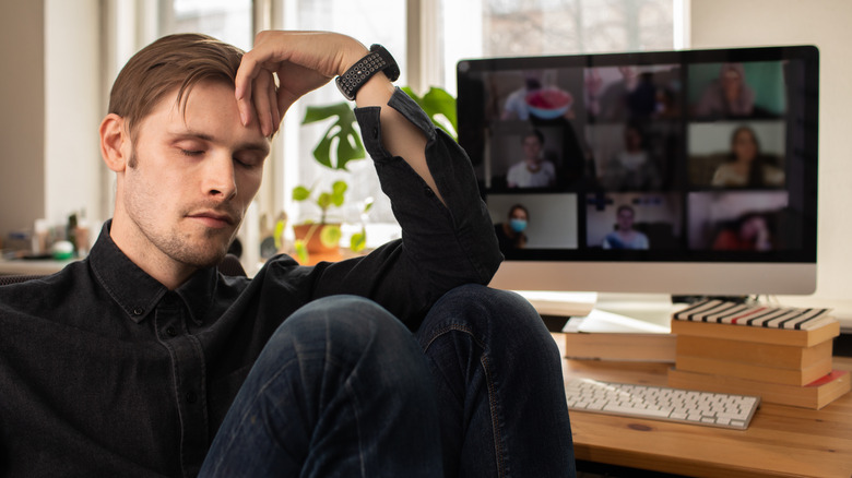 A man turning his head away from his computer that's set up for a telework conference