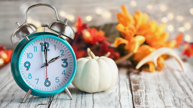 small table clock next to pumpkins and fall leaves