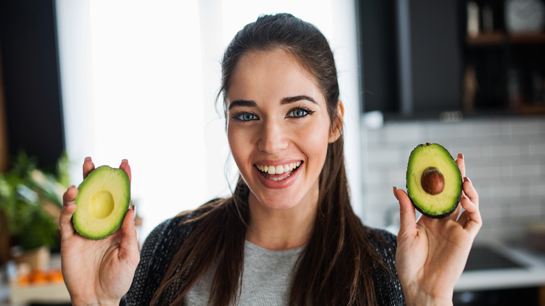 smiling woman holding a sliced avocado