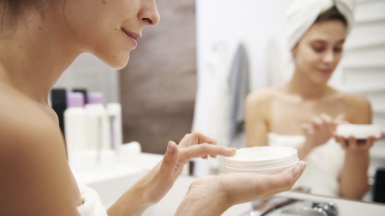 A woman dipping her fingers into a jar of skin cream
