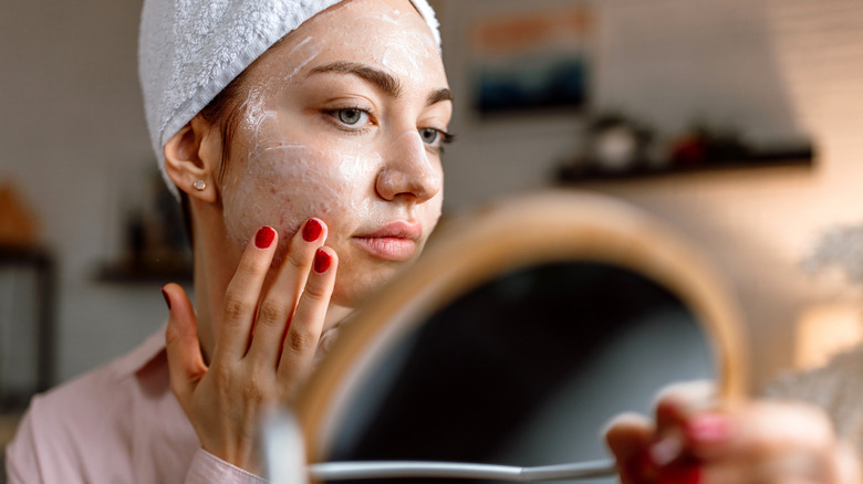 A woman applying skin cream while looking in the mirror