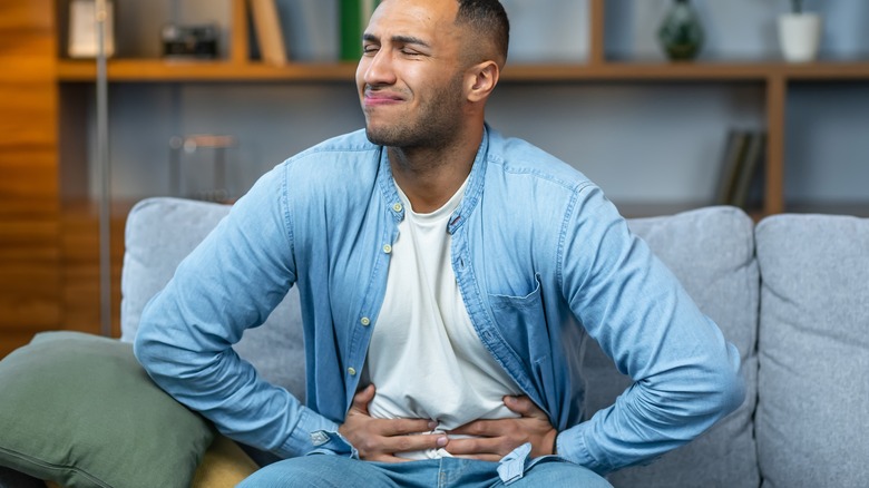 Wincing man on couch holding stomach