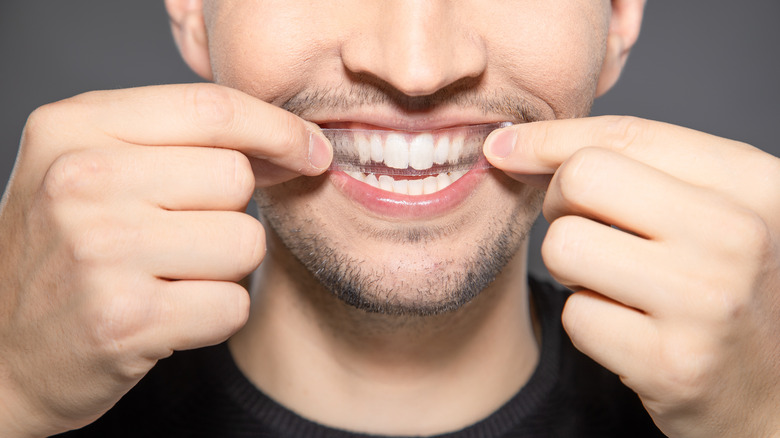 A man places a whitening strip on his teeth